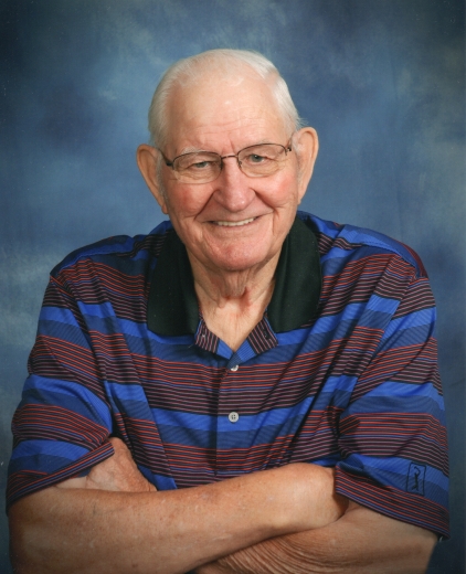 Paul smiles with his arms crossed. He is wearing a striped polo in front of a blue screen.