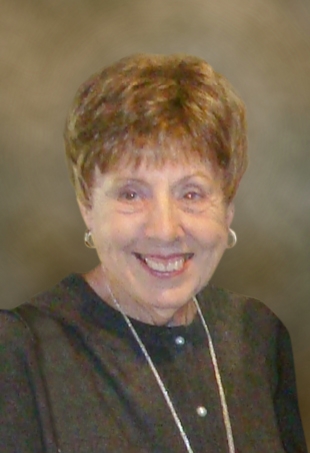 Carol smiles brightly. She wears a neutral blouse in front of a beige backdrop.