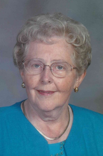 Eunice smiles for a professional photo, wearing glasses, a blue blouse and simple jewelry.