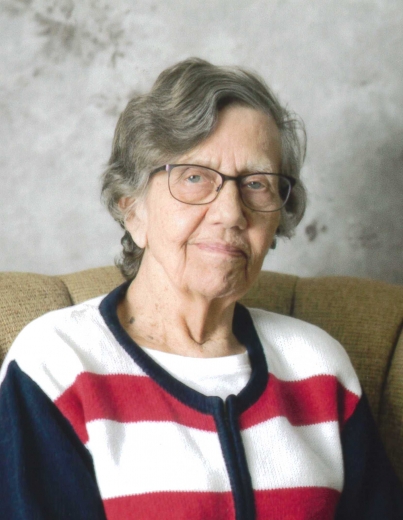 Sharon smiles for a photo, wearing glasses and a striped cardigan.