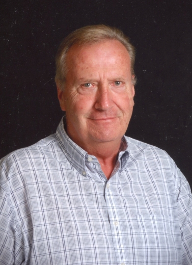 The late Dale Heitland wears a light blue plaid shirt while smiling at the camera.